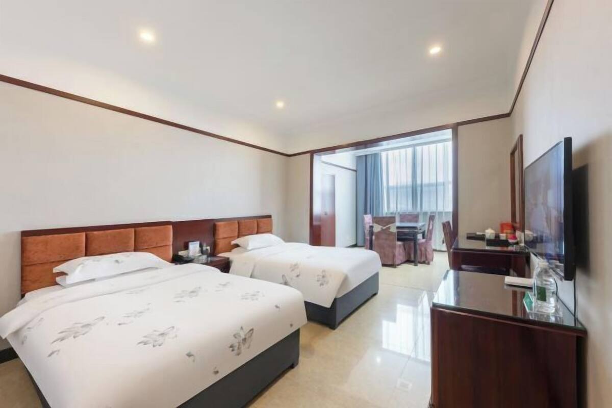Habitació d'hotel amb dos llits, un escriptori, un televisor i una finestra amb cortines.