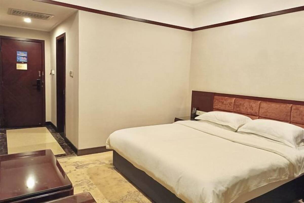 Habitació d'hotel amb llit, una petita taula de nit, una panxa de fusta i una porta.