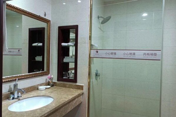 A bathroom with a large mirror, a sink, and a shower area.