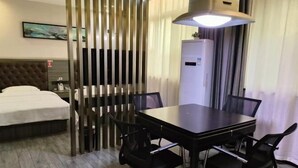 Une chambre d’hôtel comprenant un lit, une table à manger avec des chaises, un paravent et un réfrigérateur.