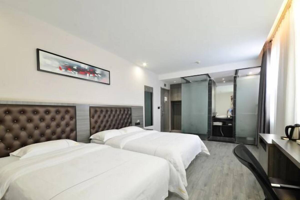 A hotel room with two beds, a large mirror, a desk, and a door leading to a bathroom.
