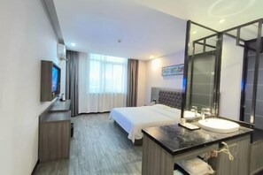 Habitación de hotel con cama, mesita de noche con espejo, televisor y ventana con cortinas.