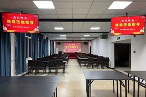 A conference room with rows of tables and chairs, a projection screen, and red banners. - Jichu hotel (Jingzhou ocean world store) (Jingzhou)