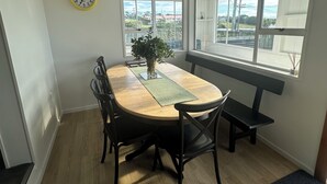 A dining area with a round table, black chairs, a bench, a clock, and large windows offering a view of the outside. - Life by the sea! Enjoy tranquil views and all-day sun. (Kakanui)