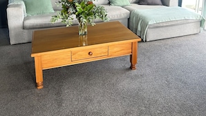 A living room with a grey sofa, a wooden coffee table, and a vase with green plants. - Life by the sea! Enjoy tranquil views and all-day sun. (Kakanui)