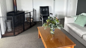 A living room with a fireplace, a sofa, a coffee table, and a door. - Life by the sea! Enjoy tranquil views and all-day sun. (Kakanui)