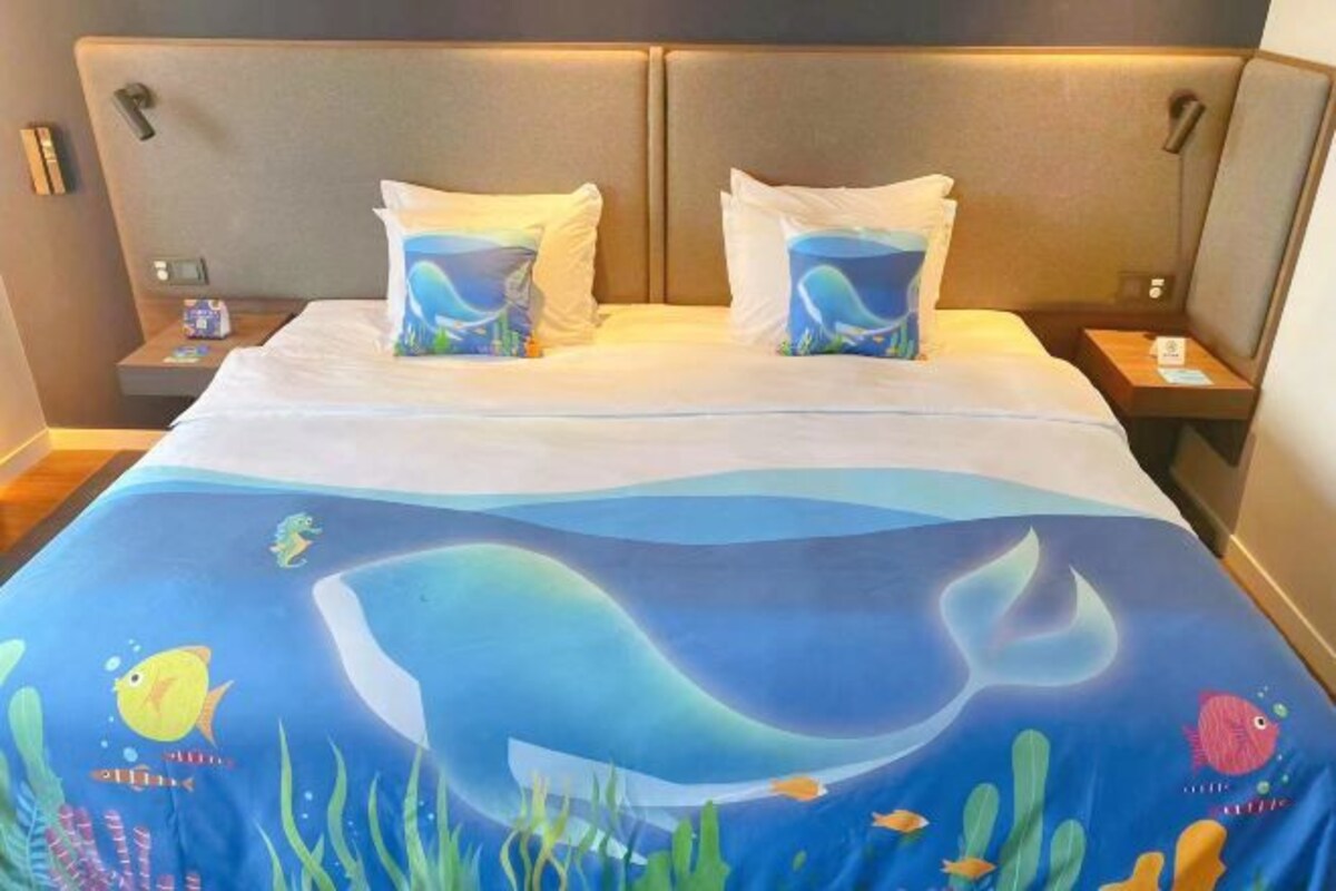 Camera d'albergo con un letto coperto da una tenda con motivi marini blu, due cuscini, un comodino e un tavolino.