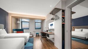 A hotel room with two beds, a desk, a chair, a TV, and a view of the city.