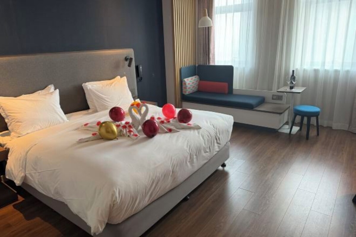 Un letto rifatto con lenzuola bianche, una testata e un comodino con una lampada.