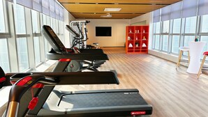 A gym with treadmills, a wall-mounted TV, and a red shelving unit with decorative items. - Holiday Inn Express Rongcheng Science And Technolo (Weihai)