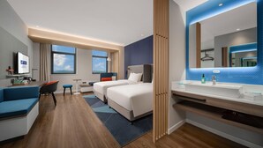 Una habitación de hotel moderna con una cama grande, un escritorio con una silla, un sofá, un baño con un espejo amplio y vistas al cielo.