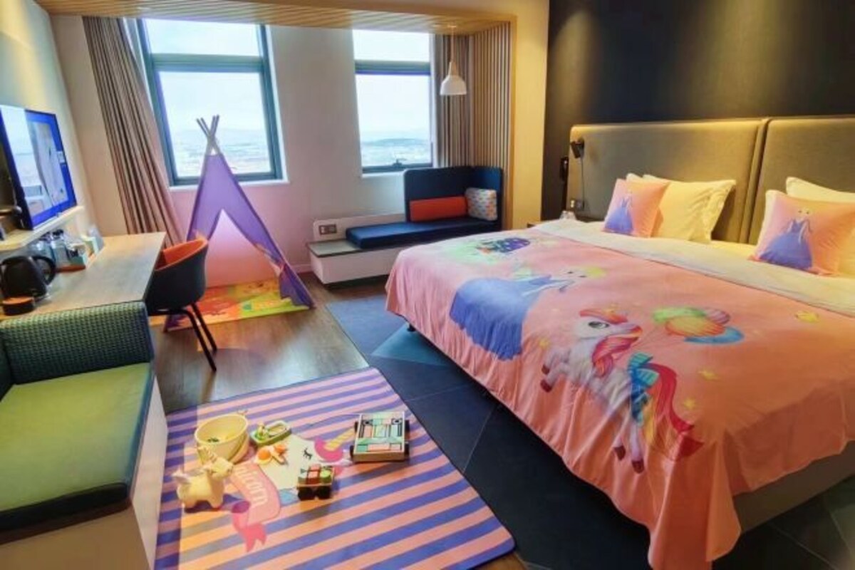 Una camera d'albergo con un letto, una scrivania, una sedia, una finestra con vista e un tappeto colorato.
