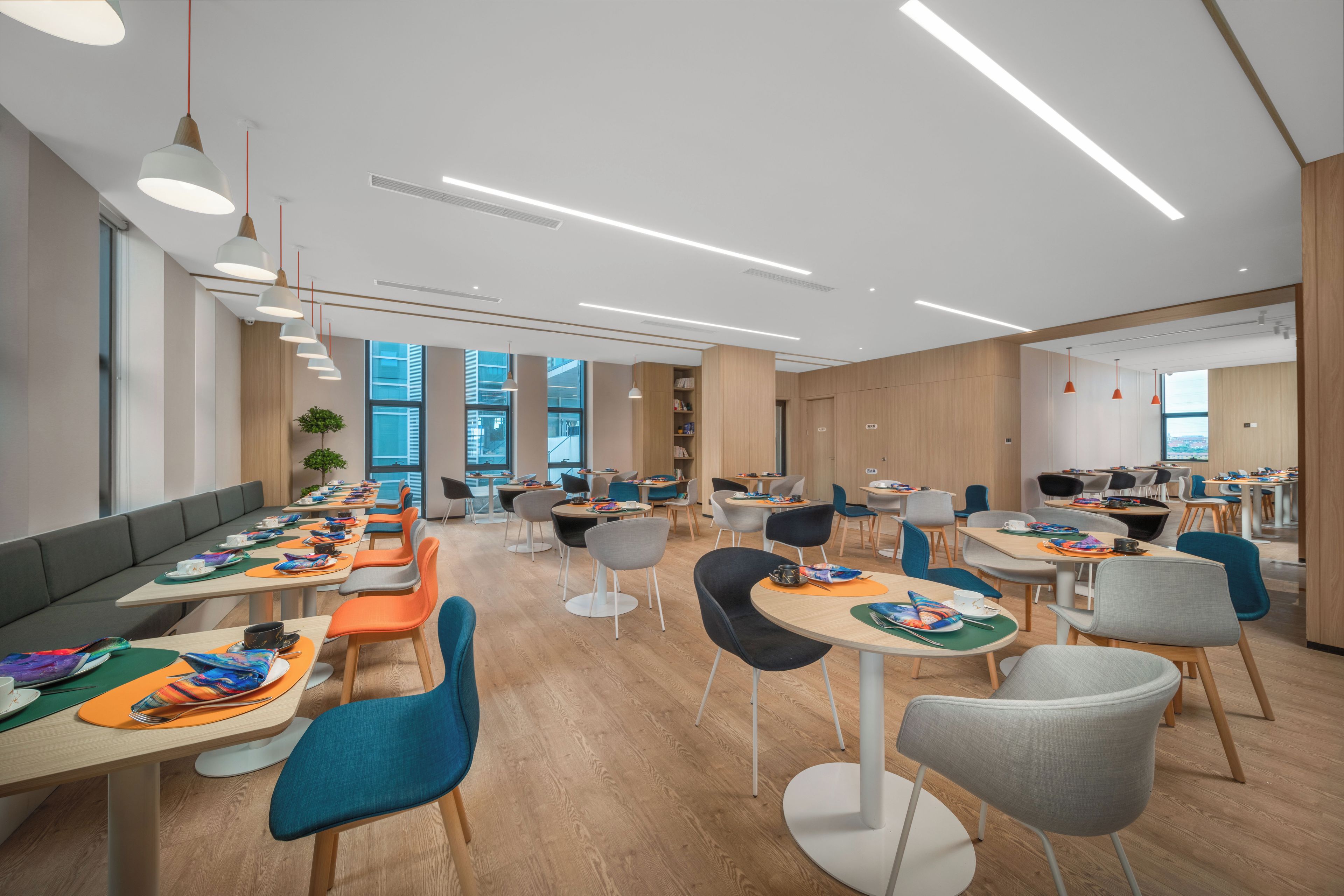 A modern dining area with long tables, colorful chairs, and pendant lighting.