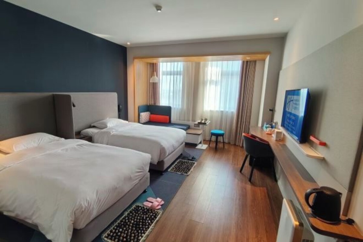 Camera d'albergo con due letti, una scrivania, una sedia, una televisione e una finestra con tende.