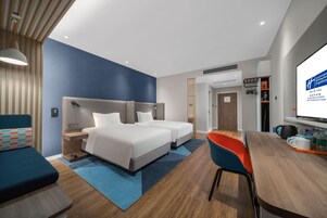 Habitación de hotel con dos camas, un escritorio, una silla, un televisor y una estantería.
