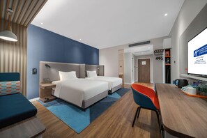 Habitación de hotel con dos camas, un escritorio, una silla, un televisor y una estantería.