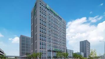 Een modern hotelgebouw met een opvallend groen bord, meerdere verdiepingen en een heldere lucht.