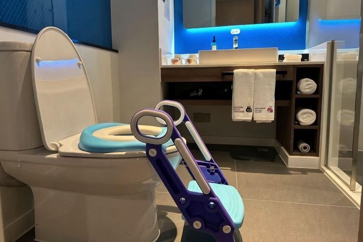 A modern bathroom with a toilet, a blue seat, a glass shower enclosure, and a towel rack.