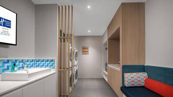 A modern hotel room with a bathroom, a washing machine, a sofa, and a wall-mounted TV.