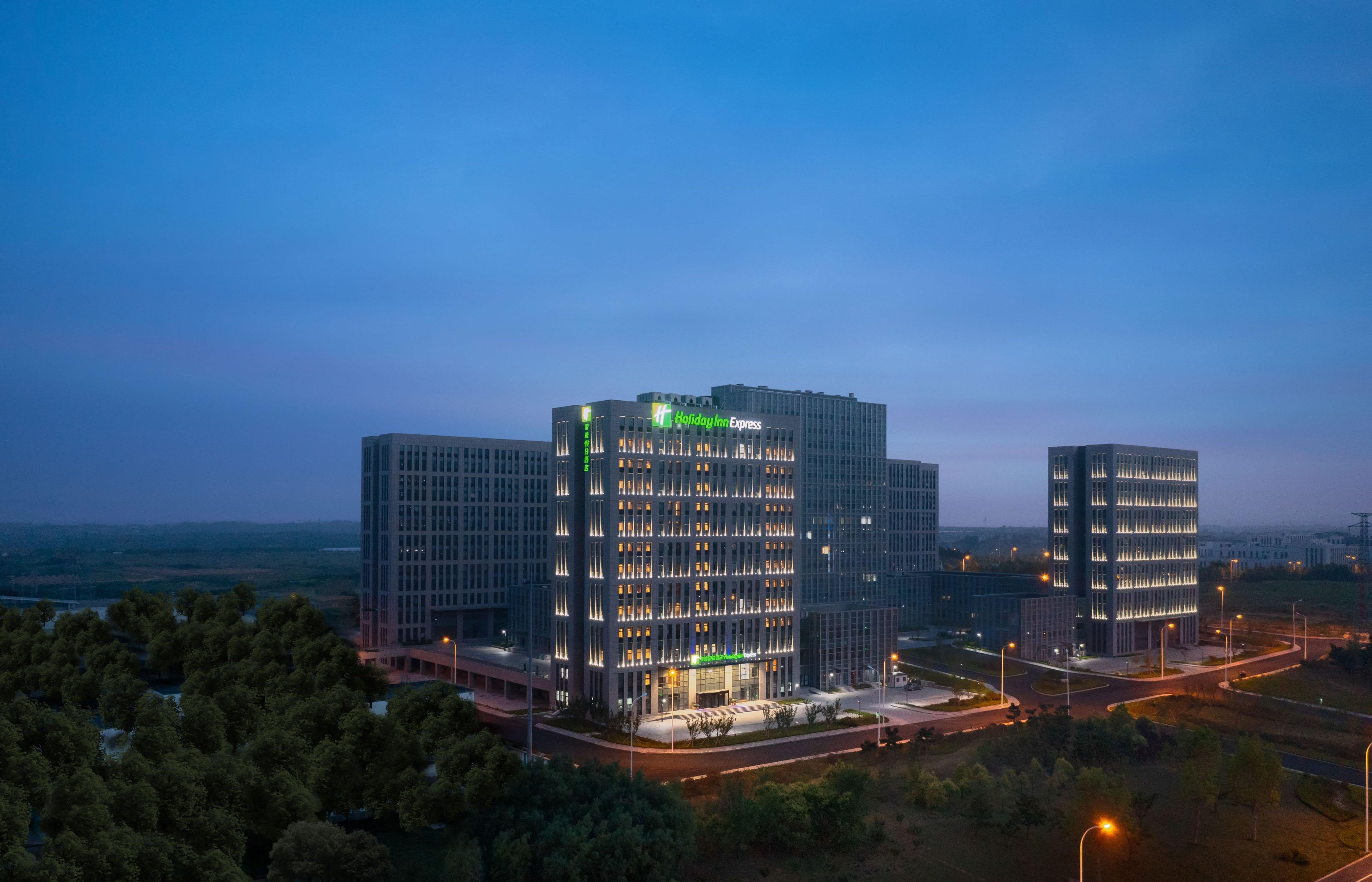 Un hotel Holiday Inn Express con fachada de vidrio moderna, varios pisos y una entrada bien iluminada.