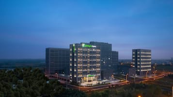 Un hotel Holiday Inn Express con fachada de vidrio moderna, varios pisos y una entrada bien iluminada.