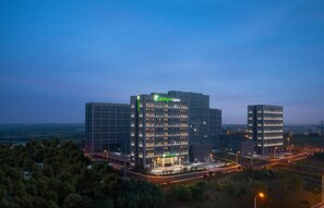 Un hotel Holiday Inn Express con fachada de vidrio moderna, varios pisos y una entrada bien iluminada.