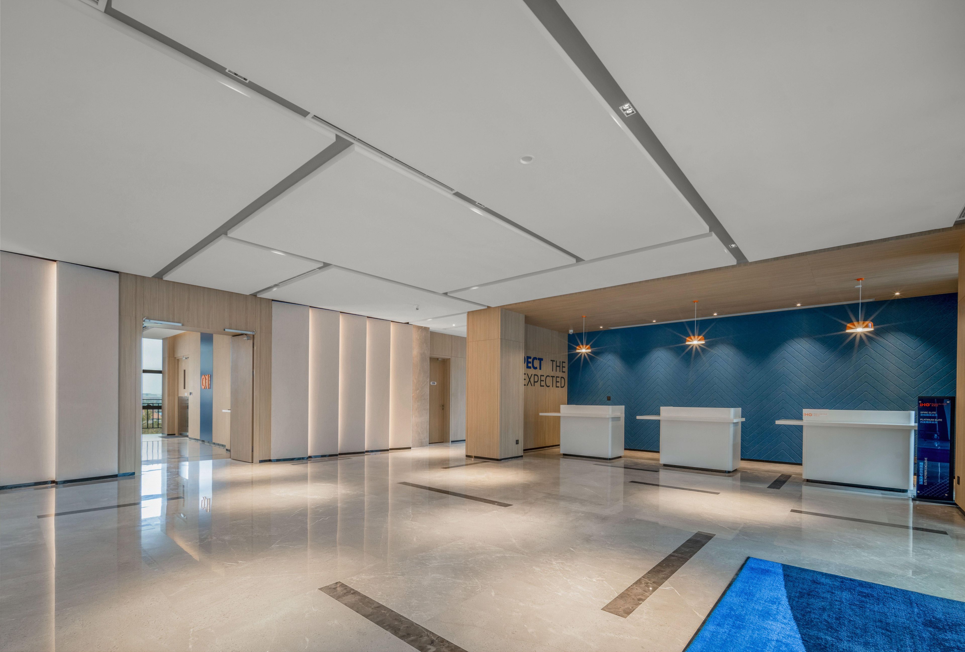 Un hall amplio con mostrador de recepción, una pared azul de acento y suelo pulido.