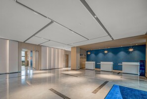 Un hall amplio con mostrador de recepción, una pared azul de acento y suelo pulido.
