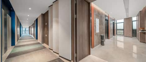A modern hotel corridor with a long hallway, wooden doors, and a tiled floor.