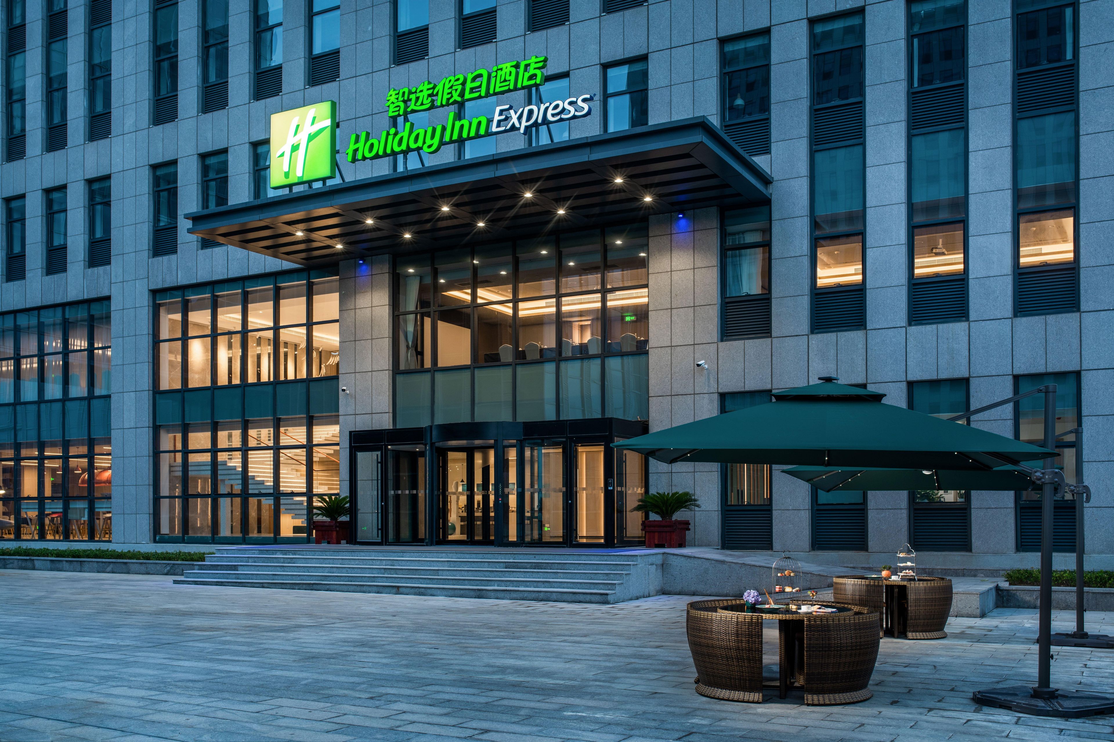 A Holiday Inn Express building with a modern facade, large glass windows, and outdoor seating area.