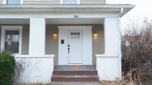 Uma casa de dois andares com porta frontal branca, número 800, e um pequeno alpendre com degraus que levam à entrada.