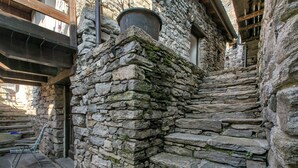 A stone staircase leading up to a wooden door, with a metal basket and a chair on the steps.