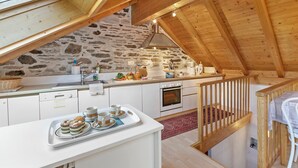 A rustic kitchen with stone walls, wooden beams, and a wooden staircase.