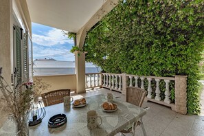 A balcony with a table set for breakfast, a wicker chair, and a white railing.