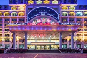 A multi-story hotel with a grand entrance, a covered area with steps, and a large arched window. - Mystic Lake Grand Hotel (Burqin)