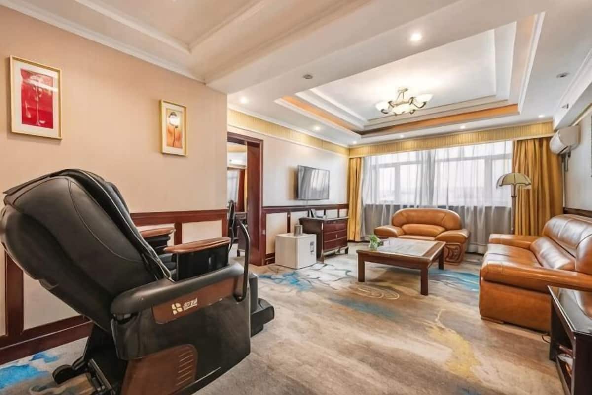 A hotel room with a massage chair, a sofa, a coffee table, a TV, and a large window with curtains.