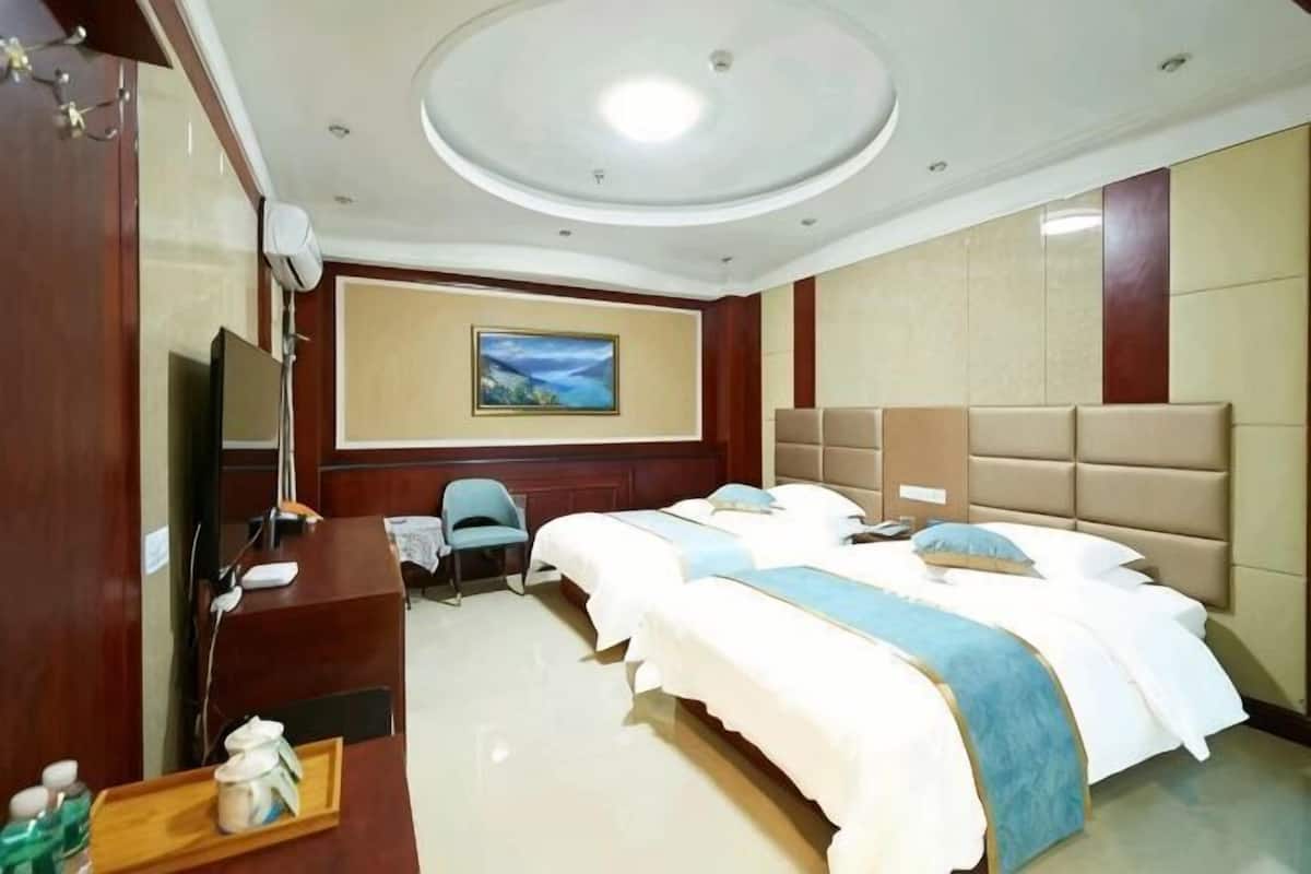 A hotel room with two beds, a desk with a computer, a TV, and a painting on the wall.