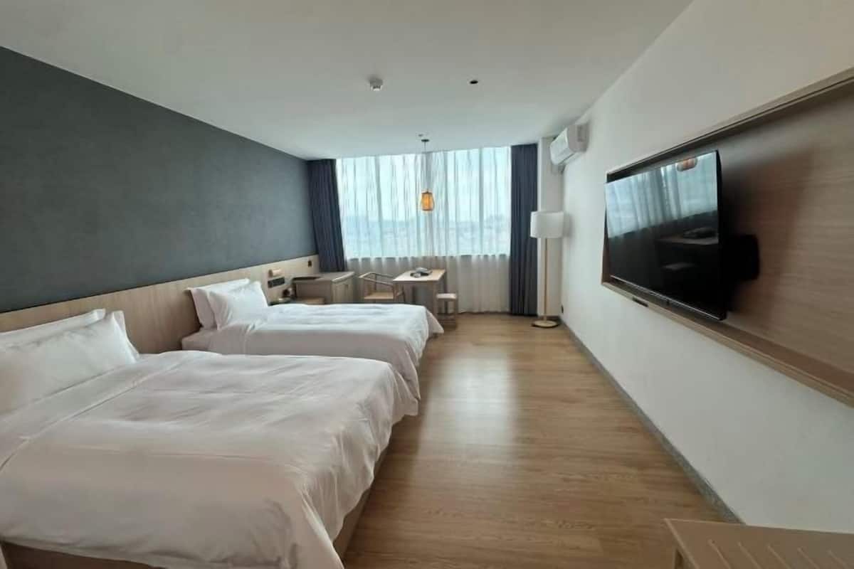 A hotel room with two beds, a desk, a chair, a TV, and a window with curtains.