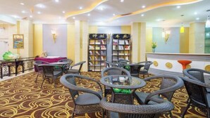 Eine Hotelhalle mit einem gemusterten Teppich, Korbmöbeln und einem Bücherregal.