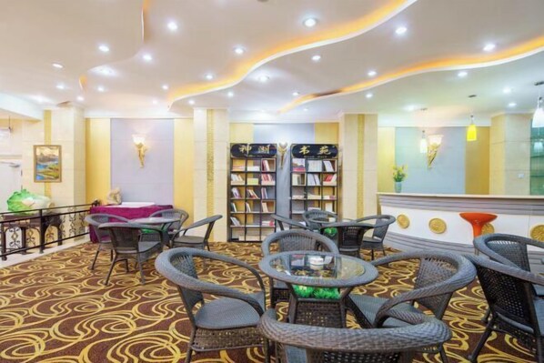 A hotel lobby with a patterned carpet, wicker furniture, and a bookshelf. - Mystic Lake Grand Hotel (Burqin)