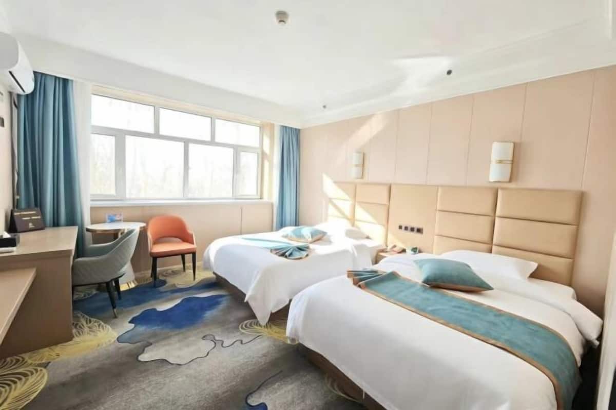 A hotel room with two beds, a desk, a chair, and a large window.