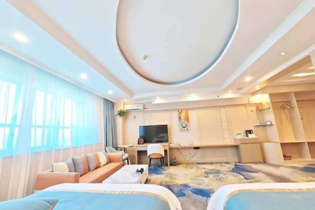 A hotel room with a sofa, a TV, a desk, and a carpet with a circular pattern.