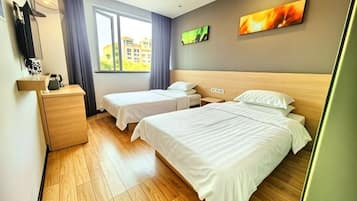 Ein Hotelzimmer mit zwei Betten, Holzboden, einem fenster mit Vorhängen, einem Flachbildfernseher und einem Gemälde an der Wand.