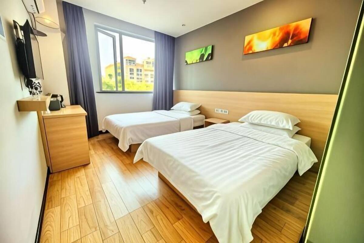 A hotel room with two beds, a wooden dresser, a window with curtains, and artwork on the wall.