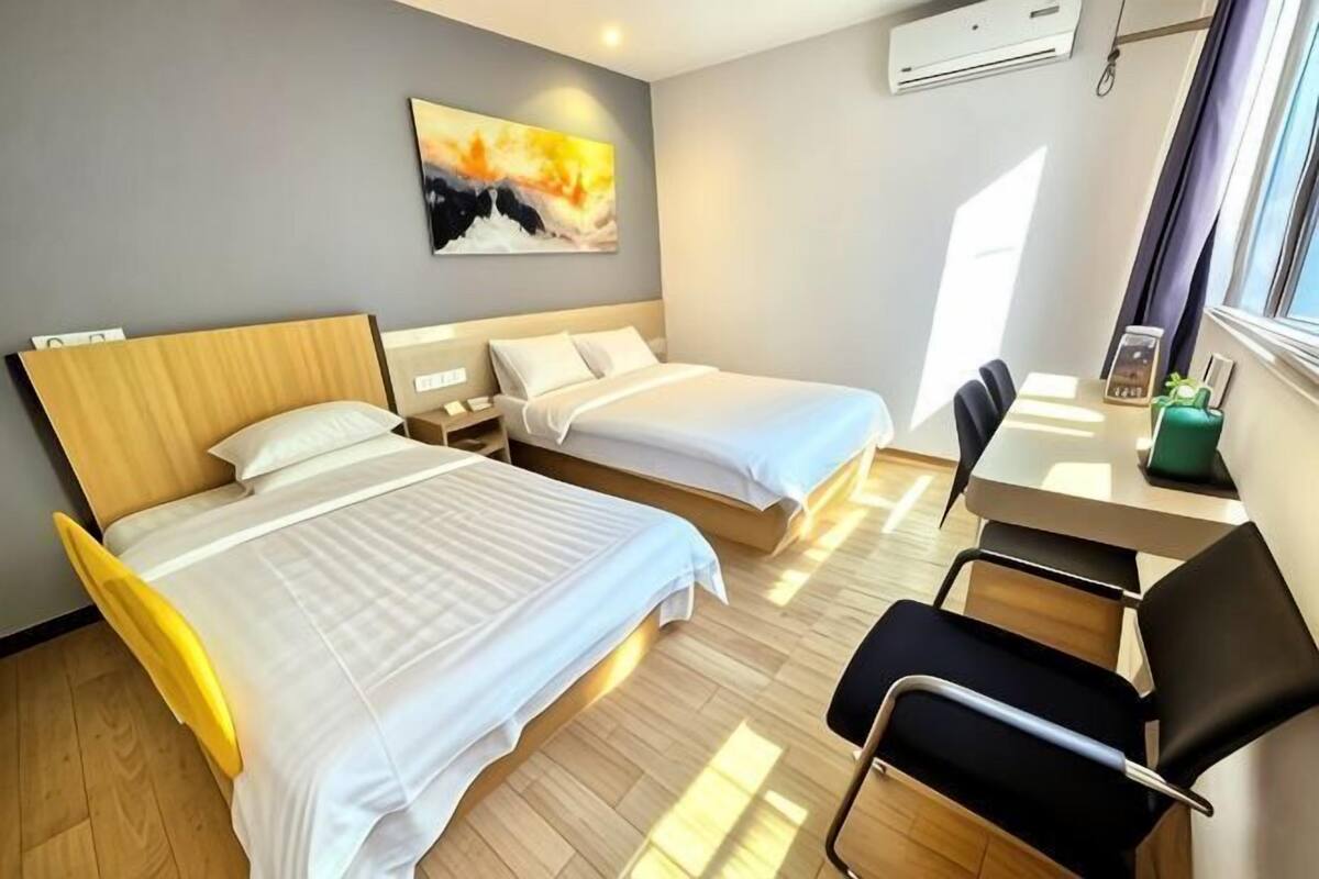 A hotel room with two beds, a desk, a chair, and a window.