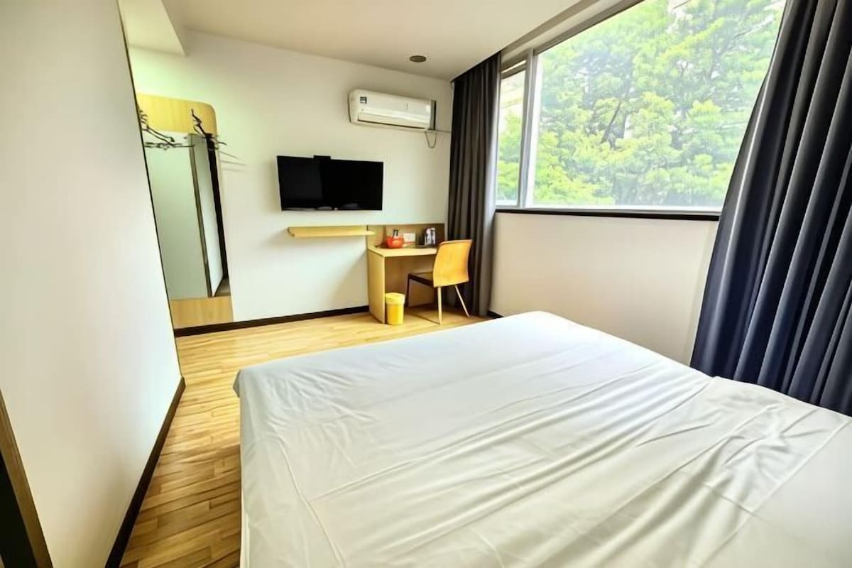A hotel room with a bed, a desk, a chair, a TV, and a window with curtains.