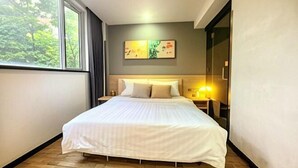 A bedroom with a large bed, a nightstand, a wall-mounted lamp, and a window with a view of trees. - Hi Inn (Shanghai Jinshan Zhujing Jinlong New Street) (Shanghai)