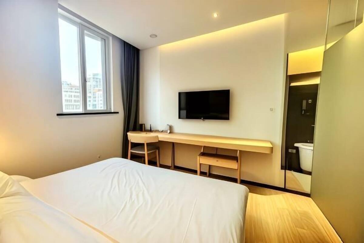 A hotel room with a bed, a desk, a TV, and a mirror.
