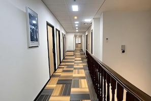 A hotel corridor with a checkered floor, doors on one side, and a railing on the other. - Hi Inn (Shanghai Jinshan Zhujing Jinlong New Street) (Shanghai)