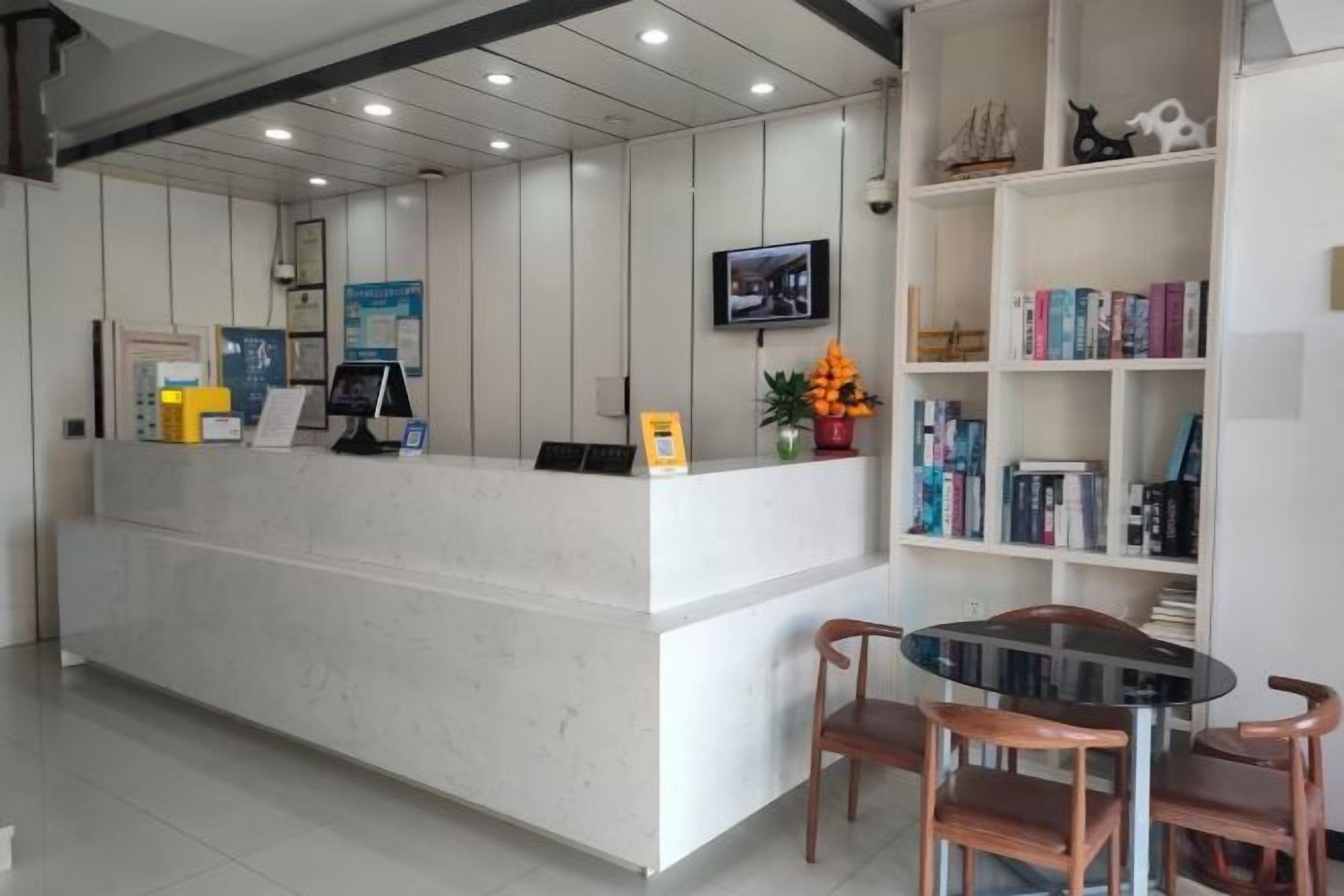 Uma área de recepção com balcão, televisão na parede e estante com livros e objetos decorativos.